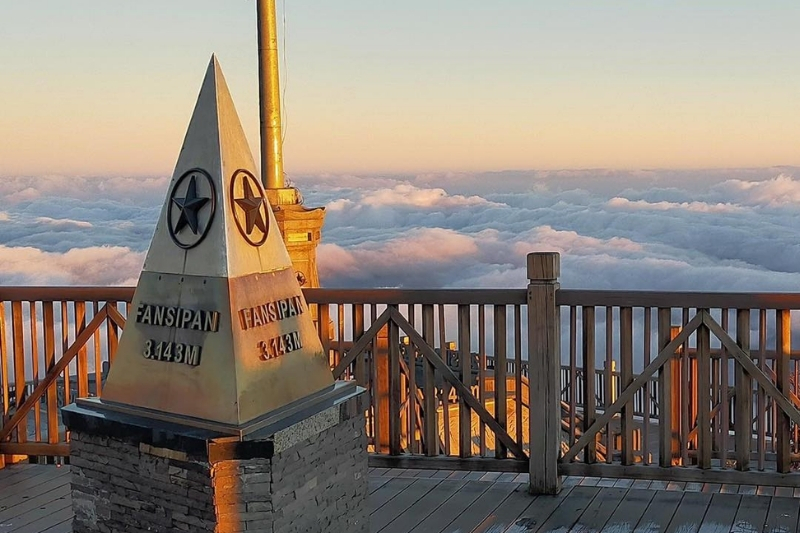 A close-up of the metal triangular milestone marking the exact peak height of Fansipan, reflecting the surrounding mountain sun.
