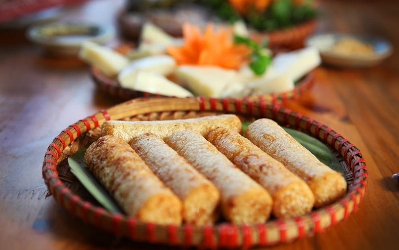 Com Lam Sapa: How Grilled Bamboo-Tube Rice Is Made Slices of roasted Com Lam sticky rice in open bamboo tubes, served on banana leaves alongside salted sesame dip.