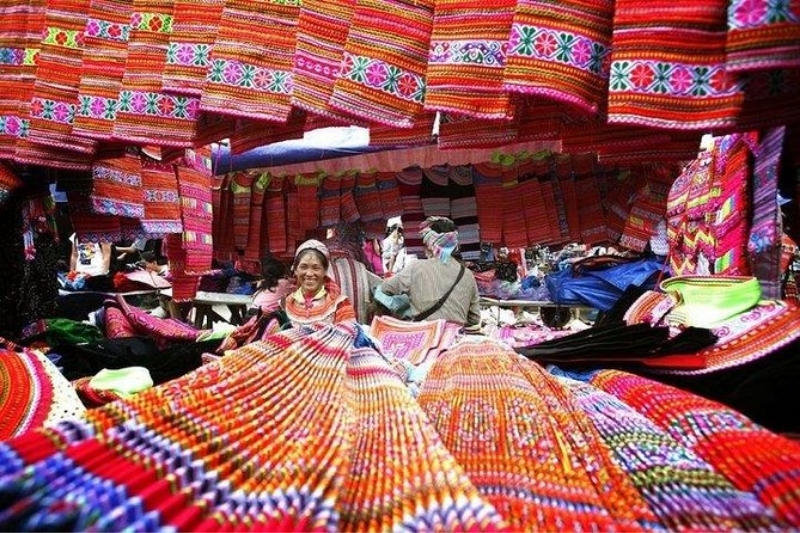 A colorful and dense display of intricately hand-woven ethnic brocade fabrics, bags, and traditional clothing at a Sapa mountain market.
