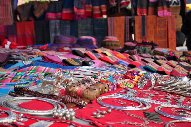 A traveler smiling while interacting politely with a local ethnic minority artisan selling handmade souvenirs at a Sapa market stall.