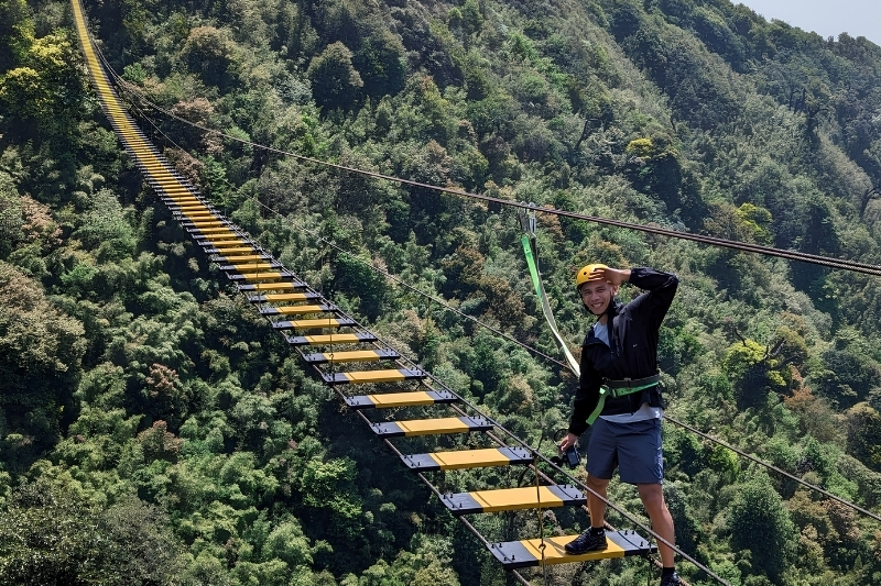 An adrenaline seeker sliding down a high-velocity zipline over the deep jungle valleys beneath the Rong May Glass Bridge.