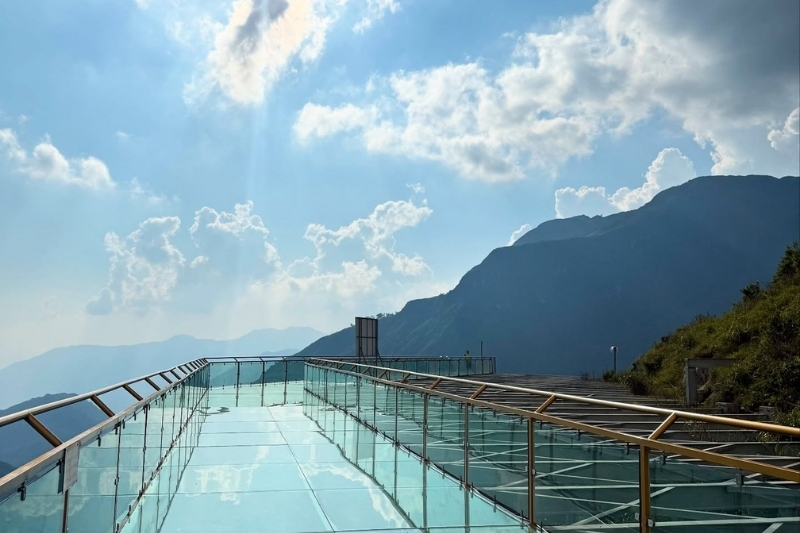 A towering, vertical transparent glass elevator shaft built flat against the sheer limestone cliffs of the Rong May tourist complex.