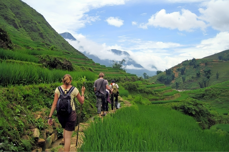 A group of international trekkers wearing hiking gear walking single file along a rugged mountain ridge overlooking deep valley passes.